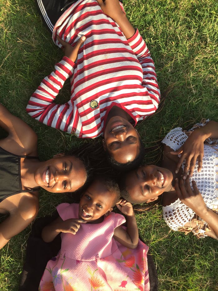 Four smiling individuals lying on the grass in Kampala, Uganda, enjoying sunny weather.