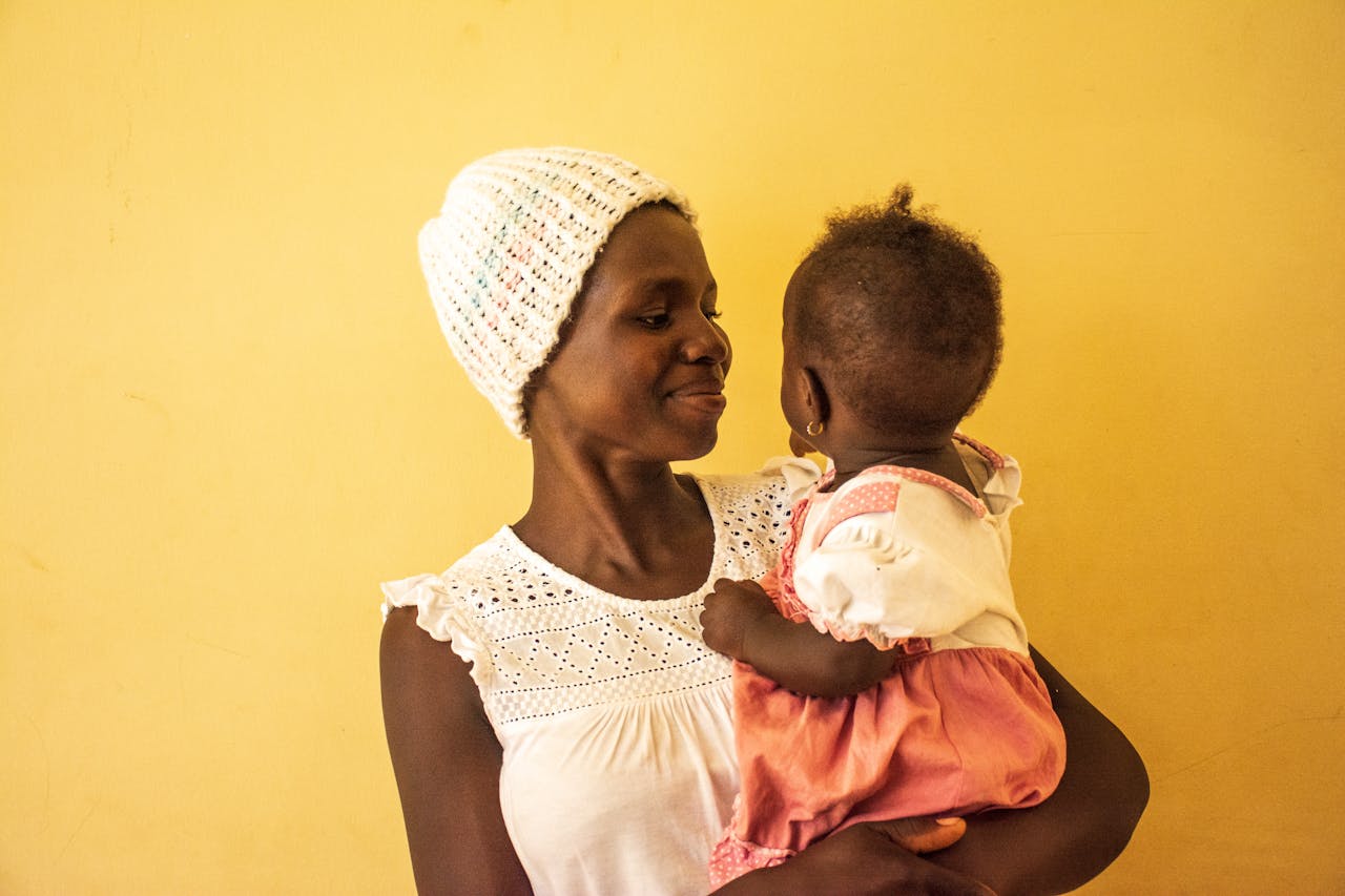 A mother lovingly holds her baby girl, capturing a tender moment indoors in Uganda.