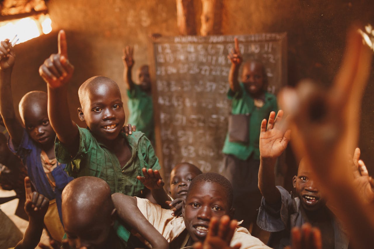 Young students in Kitgum, Uganda, enthusiastically participate in class, raising their hands with smiles.